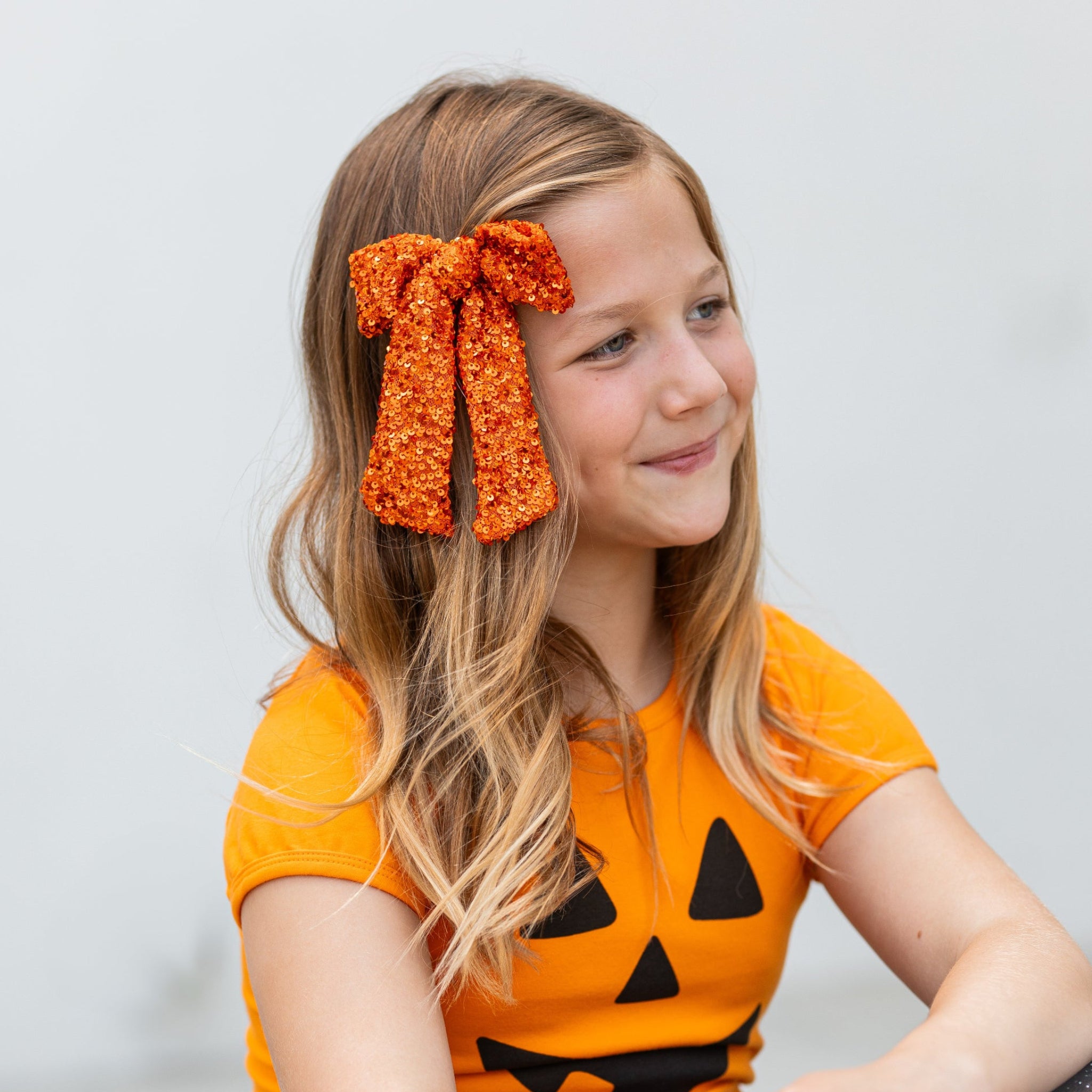 girl in orange fitted top with jack-o-lantern face design and orange oversized hair bow with sequins for Halloween