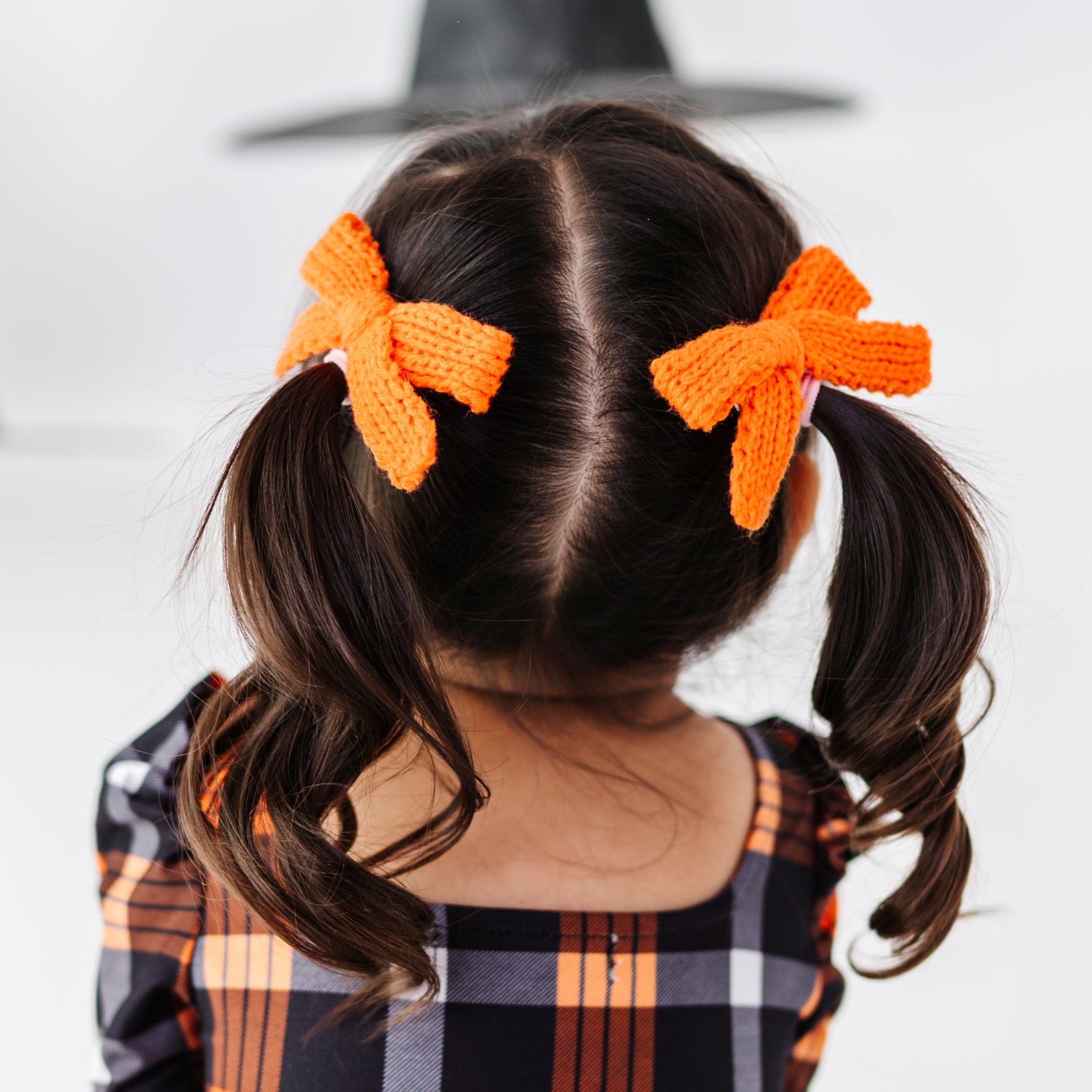 little girl in orange and black Halloween plaid dress paired with bright orange yarn knit pigtail bows on clips