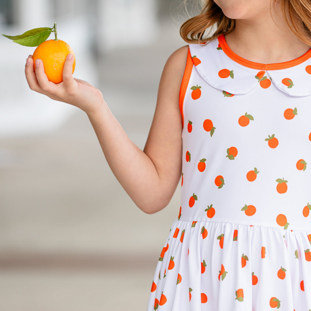 dress detail of orange print dress on little girl holding up one orange in her hand