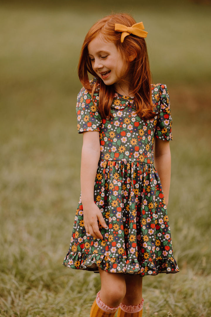 little girl in field in floral and apple print twirl dress on forest green paired with pencil design knee socks