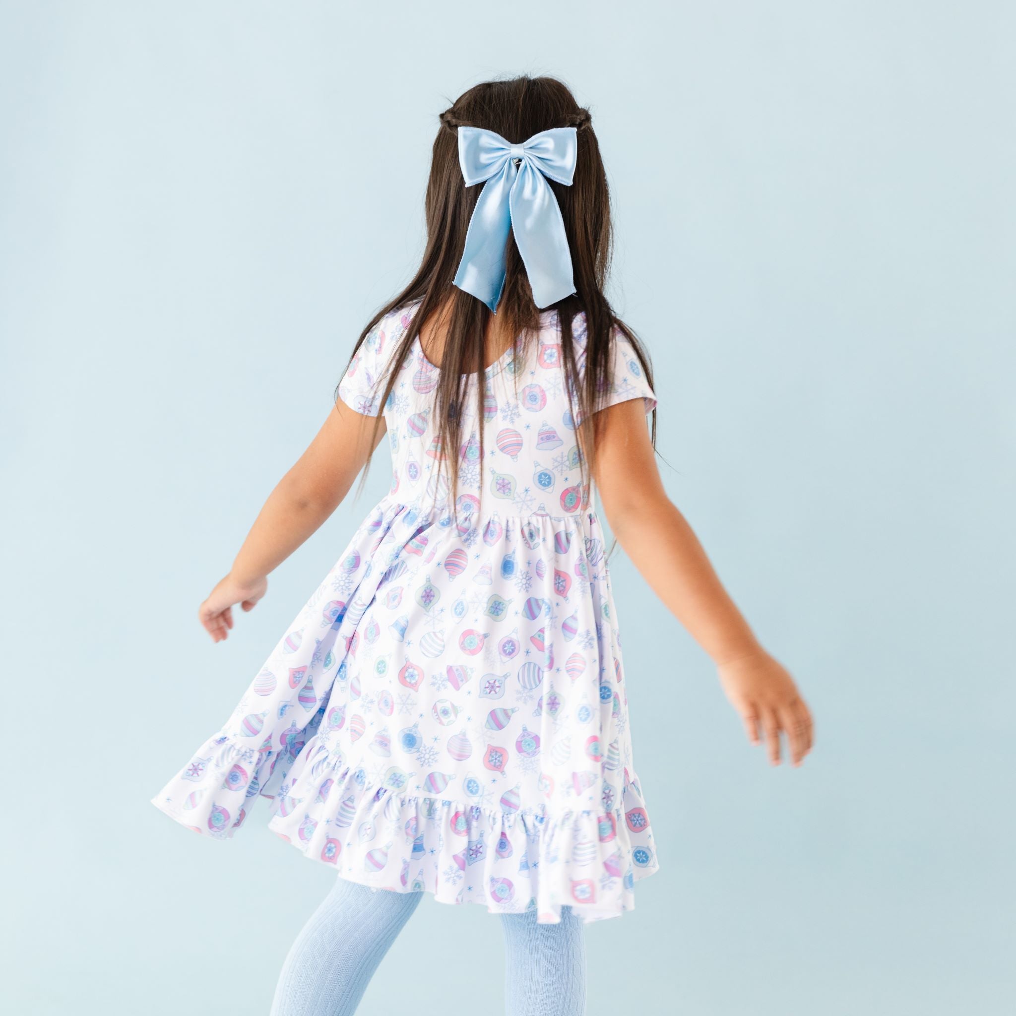 little girl in Christmas dress with pastel ornament print and matching winter blue tights and satin bow 