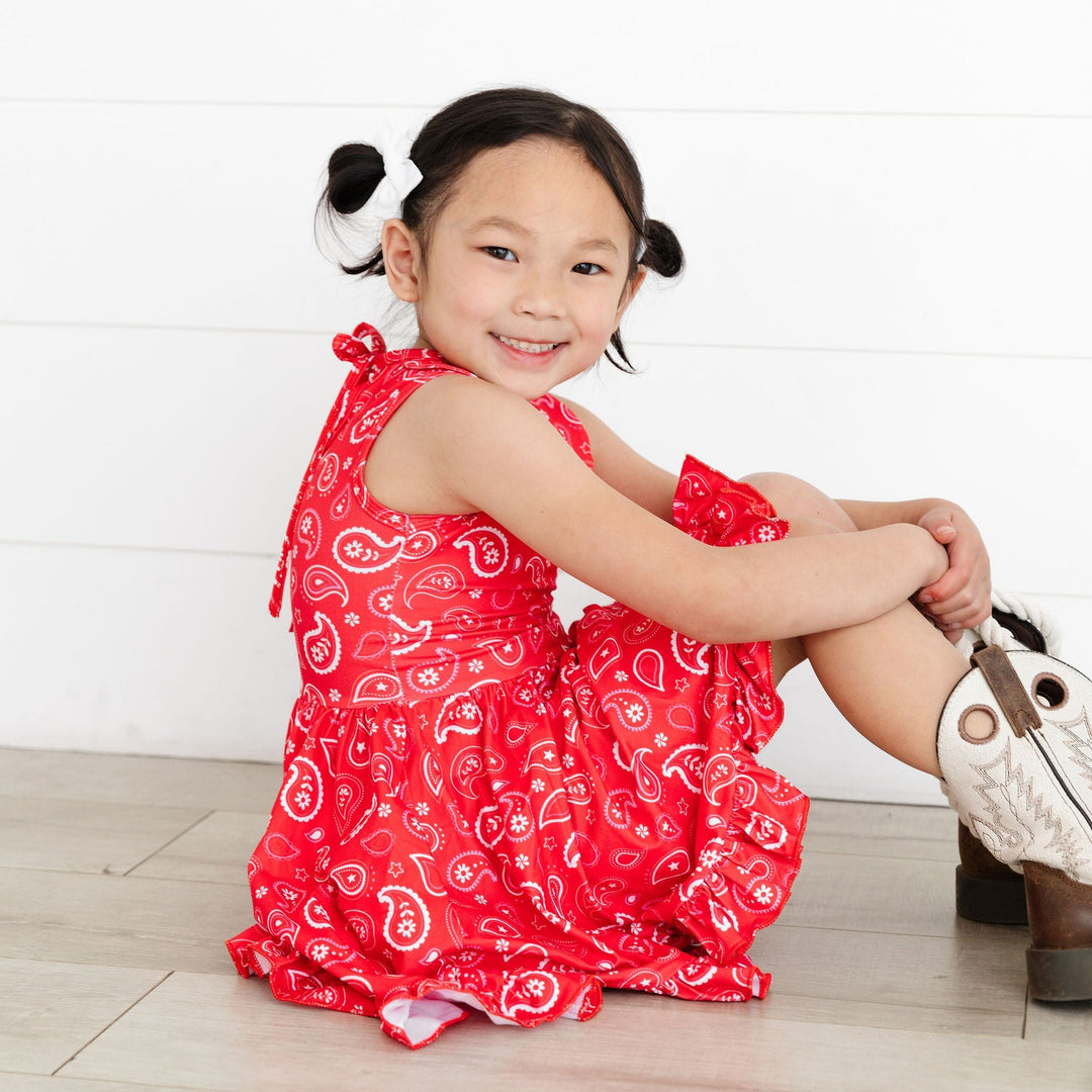 little girl sitting on floor in red paisley print dress and cowgirl boots