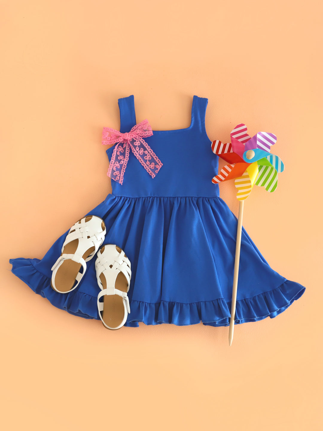 flat lay of royal blue sleeveless twirl dress paired with pink lace hair bow on clip and white sandals for summer