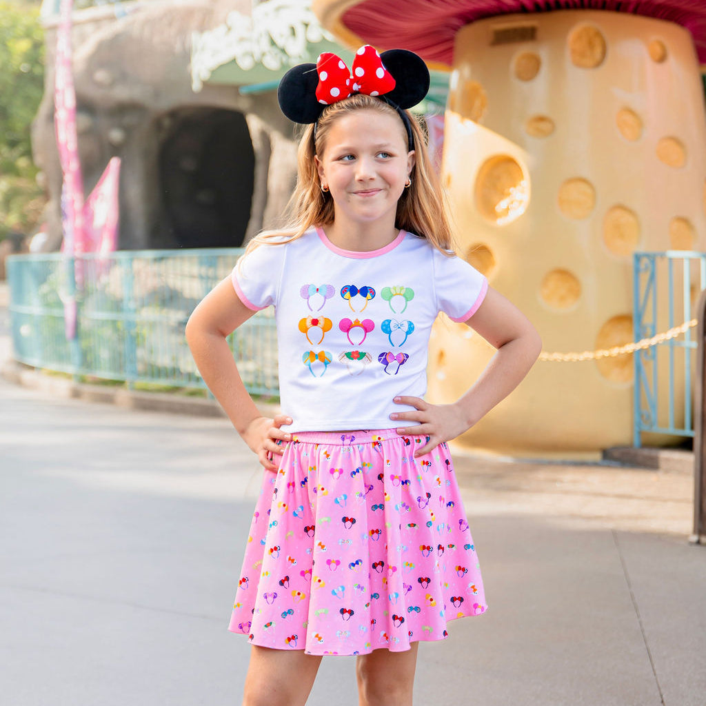 Young girl wearing a colorful shirt and pink skirt with a character-themed background