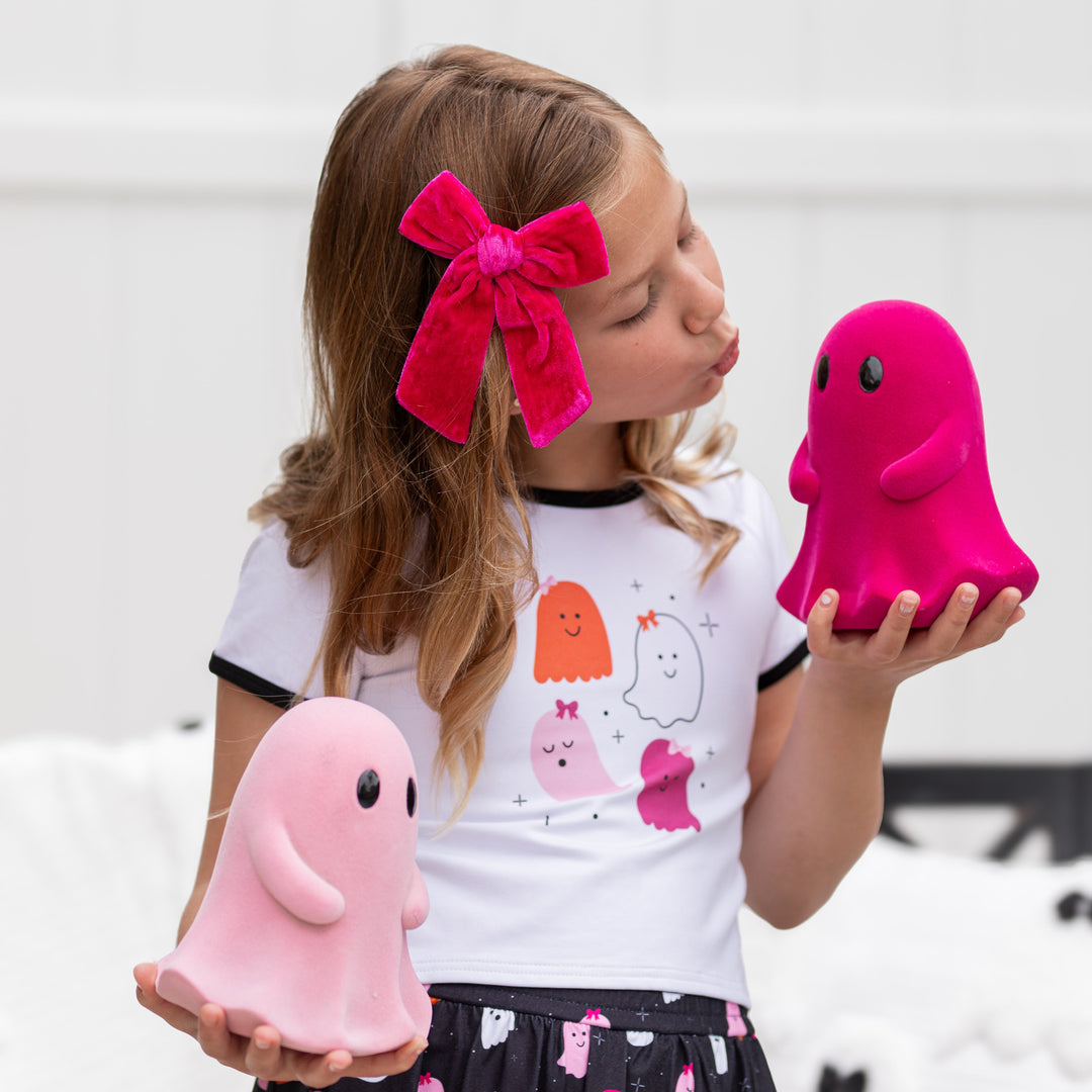 girl holding ghost decorations in ghost print tee and matching bright pink velvet bow on clip