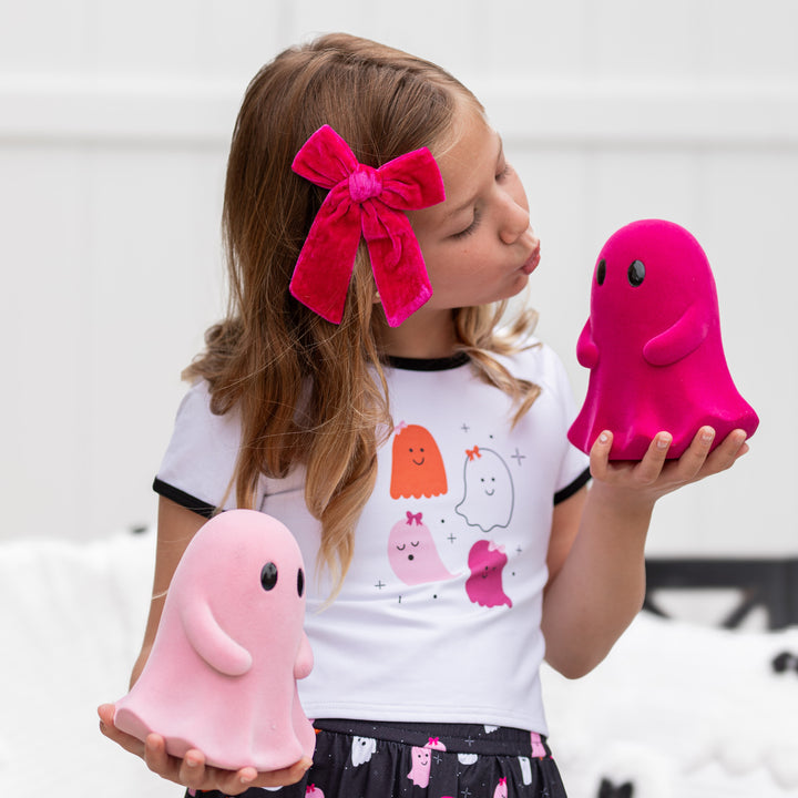 girl holding ghost decorations in ghost print tee and matching bright pink velvet bow on clip