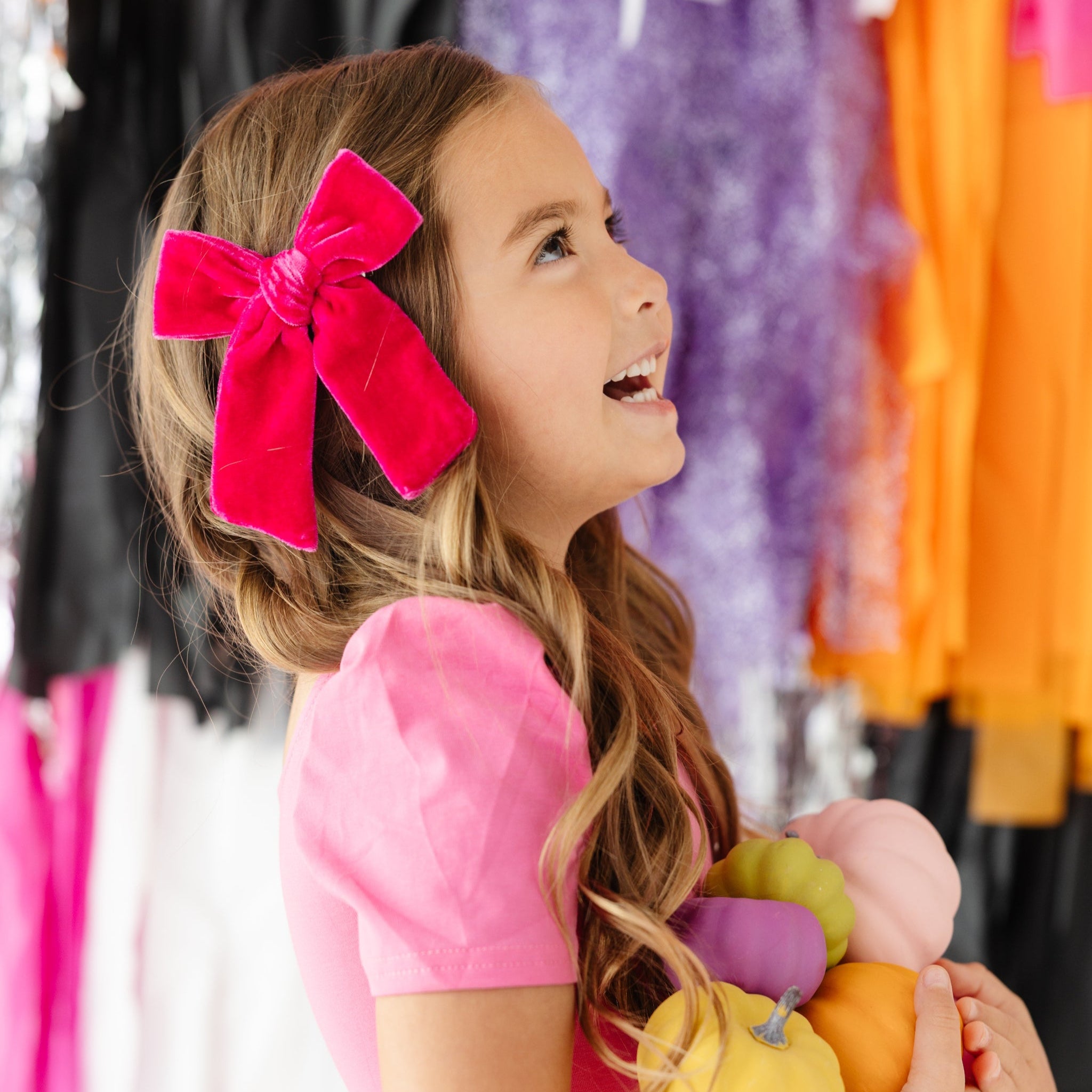 little girl holding multi-colored pumpkins in pink twirl dress and right pink velvet bow on clip for pink Halloween