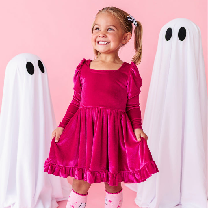young girl standing beside ghost decor in hot pink long sleeve velvet twirl dress with square neckline paired with pink ghost knee socks for Halloween