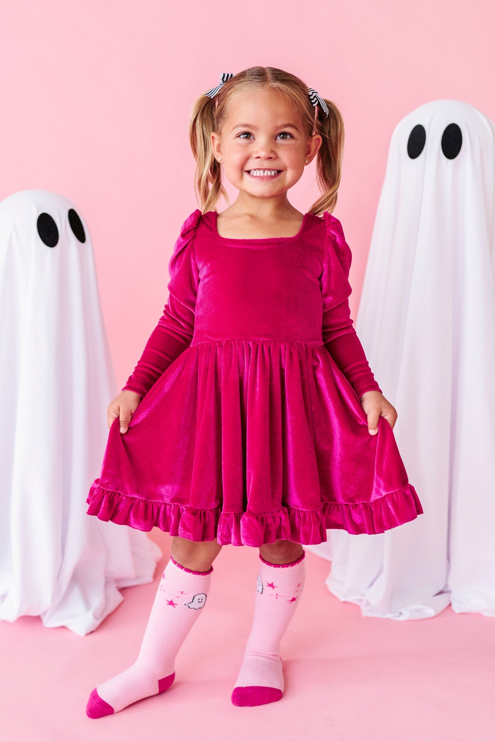 little girl standing beside sheet ghost decorations in hot pink long sleeve velvet twirl dress with square neckline paired with matching two tone pink knee socks with ghost design