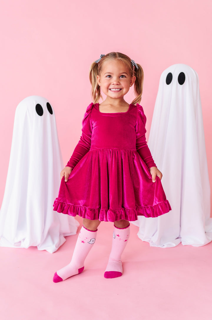 little girl standing beside sheet ghost decorations in hot pink long sleeve velvet twirl dress with square neckline paired with matching two tone pink knee socks with ghost design