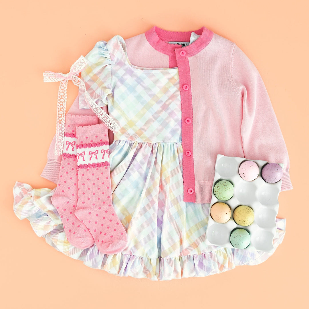 flatlay of girl's Easter outfit with pink cardigan, pastel gingham print twirl dress and matching socks and bow