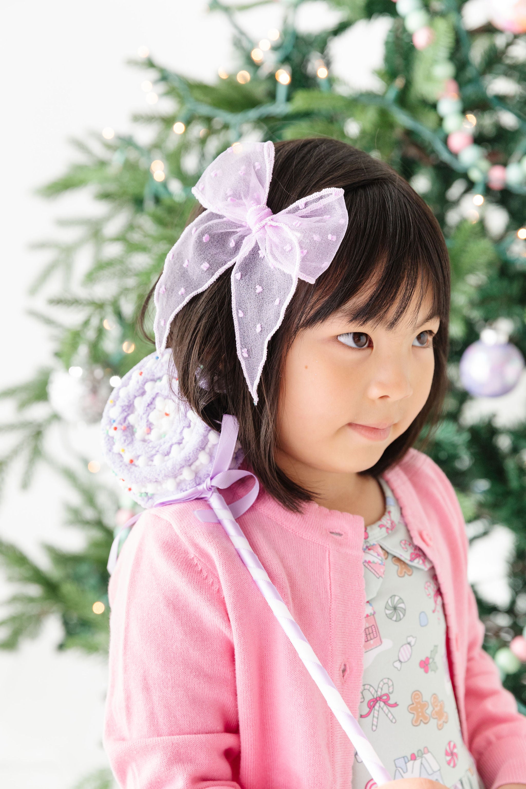 little girl wearing pastel purple sheer hair bow with candyland christmas dress and pink sweater