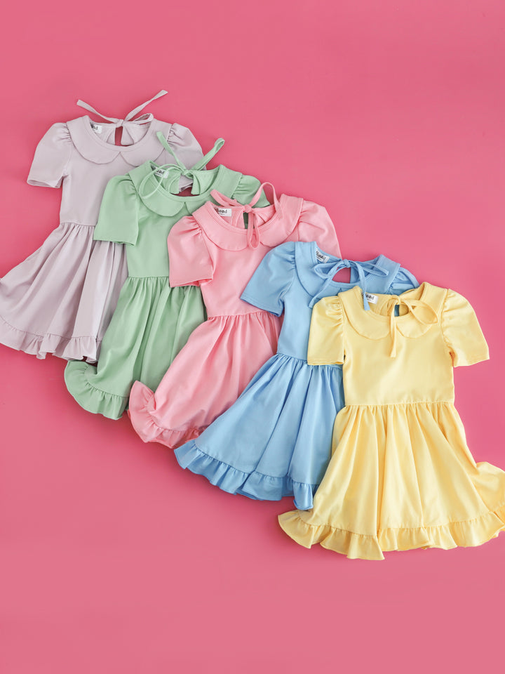 flat lay of five solid, cotton blend, pastel twirl dresses with peter pan collars for girls' spring collection in lavender, mint, blossom pink, bluebell and sunshine yellow