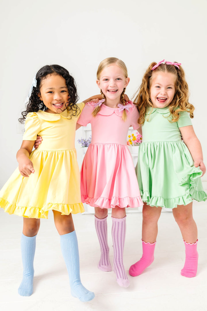 three girls in solid pastel yellow, pink and green twirl dresses with peter pan collars and mix and match pastel socks for spring