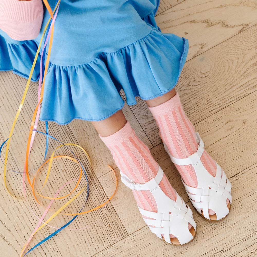 little girl sitting on floor in blue dress wearing peach and pink vertical striped midi socks and white sandals