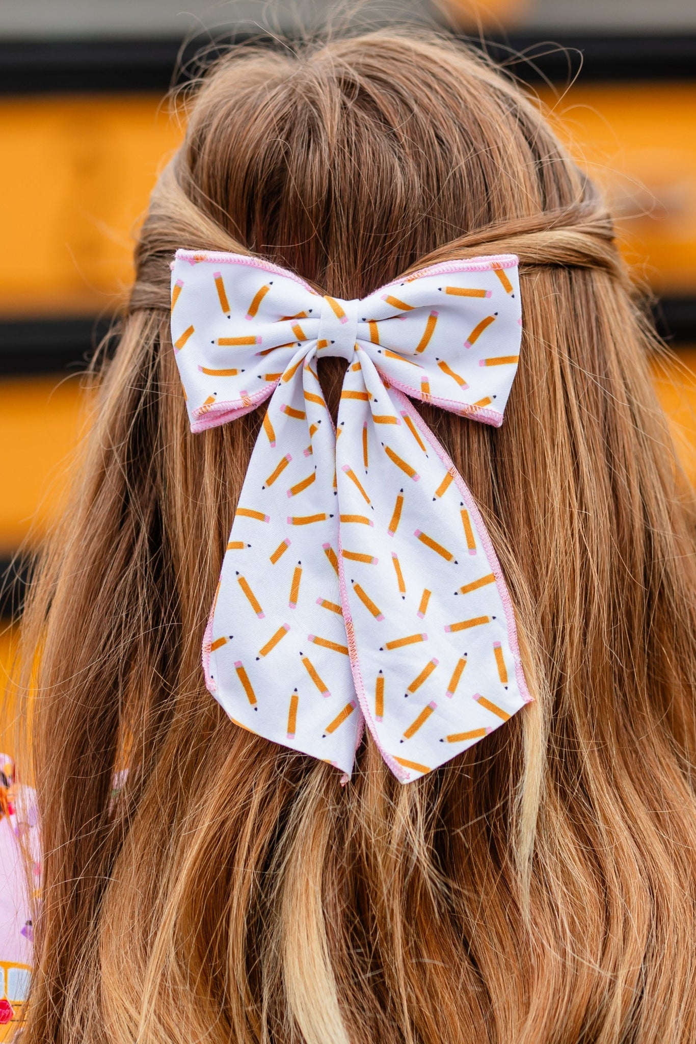 little girl in front of school bus wearing white fabric double bow with pencil print and pink trim paired with school themed pink twirl dress