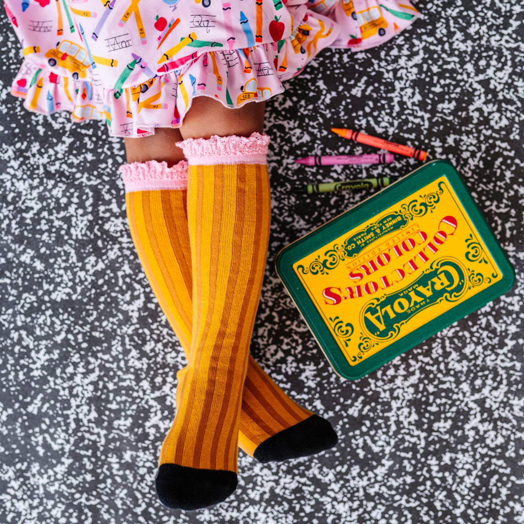 little girl with box of vintage crayons in pencil inspired knee socks with pink lace trim and matching pink first day of school dress