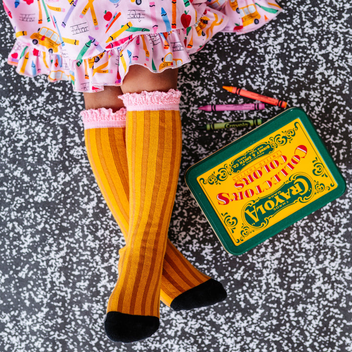 little girl with box of vintage crayons in pencil inspired knee socks with pink lace trim and matching pink first day of school dress