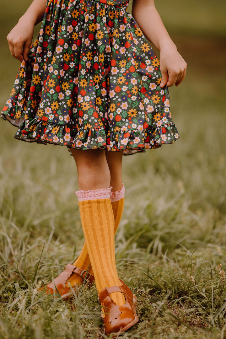 little girl in brown mary janes and pencil themed knee socks paired with green floral and apple print twirl dress