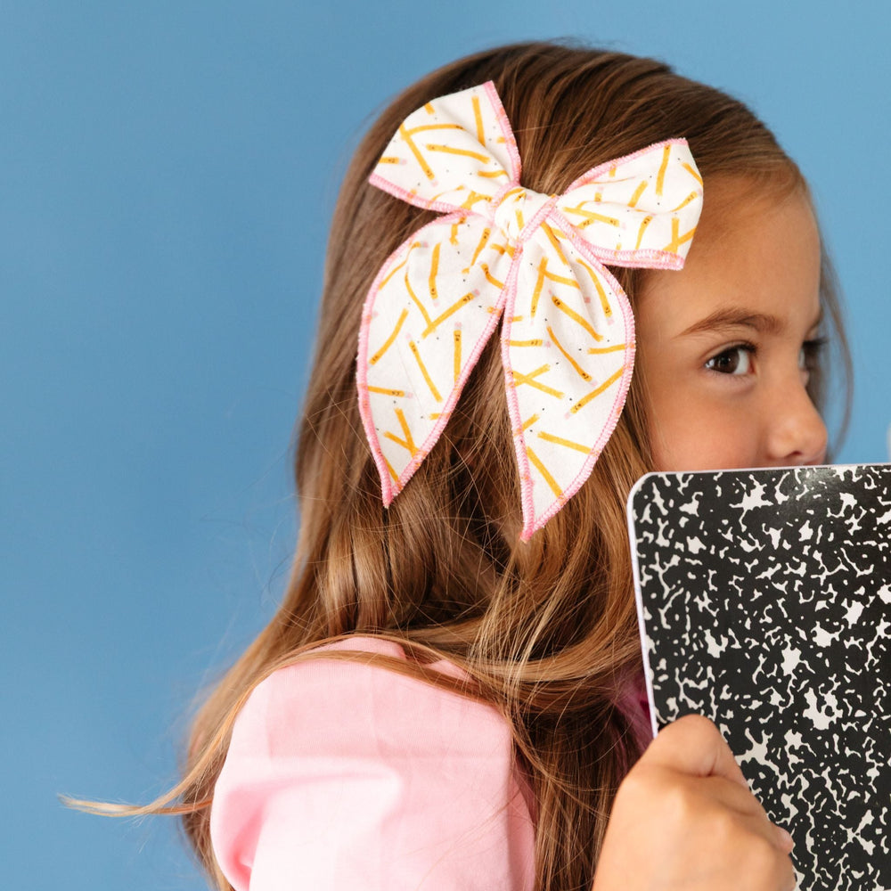 little girl holding school notebook in pink dress and matching pencil bow with pink trim