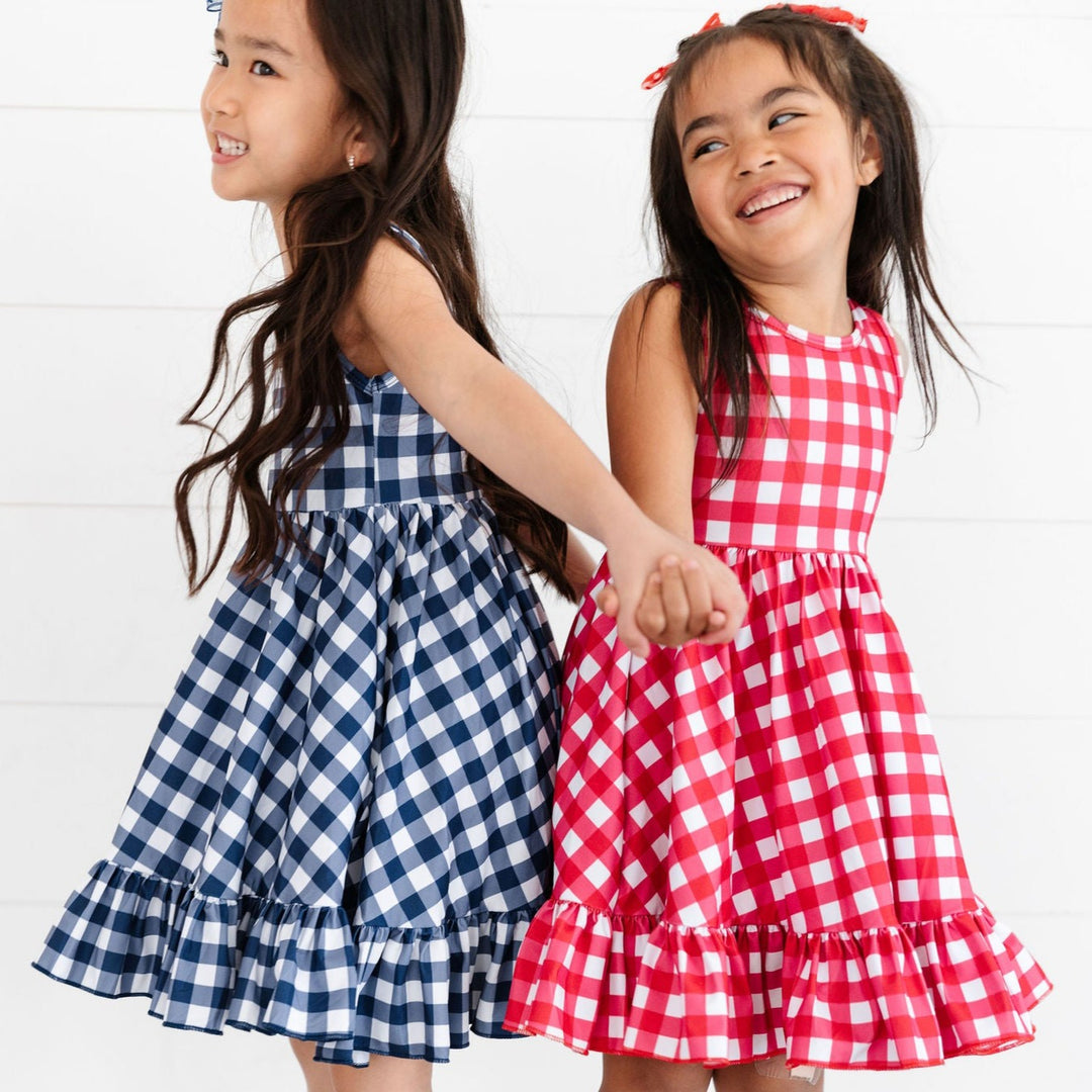 navy and red picnic plaid twirl dresses on two girls standing back to back and holding hands