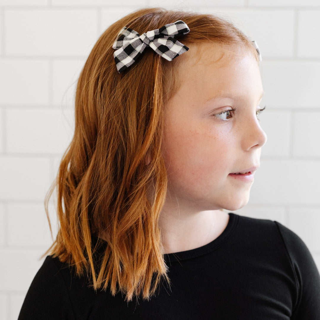 little girl looking to side wearing black solid dress and black and white gingham hair bow
