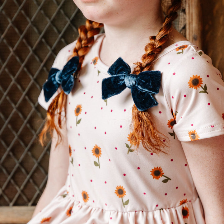little girl in sunflower print dress with braided pigtails and sapphire blue velvet pigtail bows clipped in