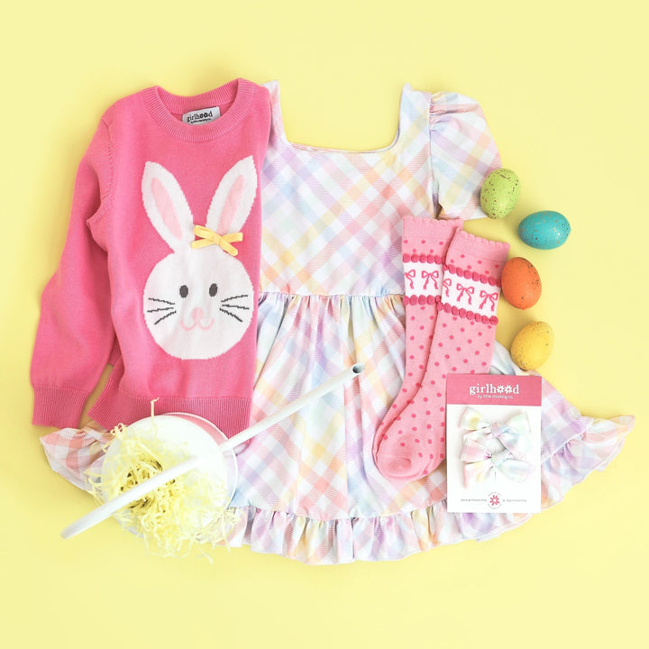 girls easter outfit of pastel gingham twirl dress, matching pigtail bows, pink sweater with bunny on it, pink socks with bows and dots on them.