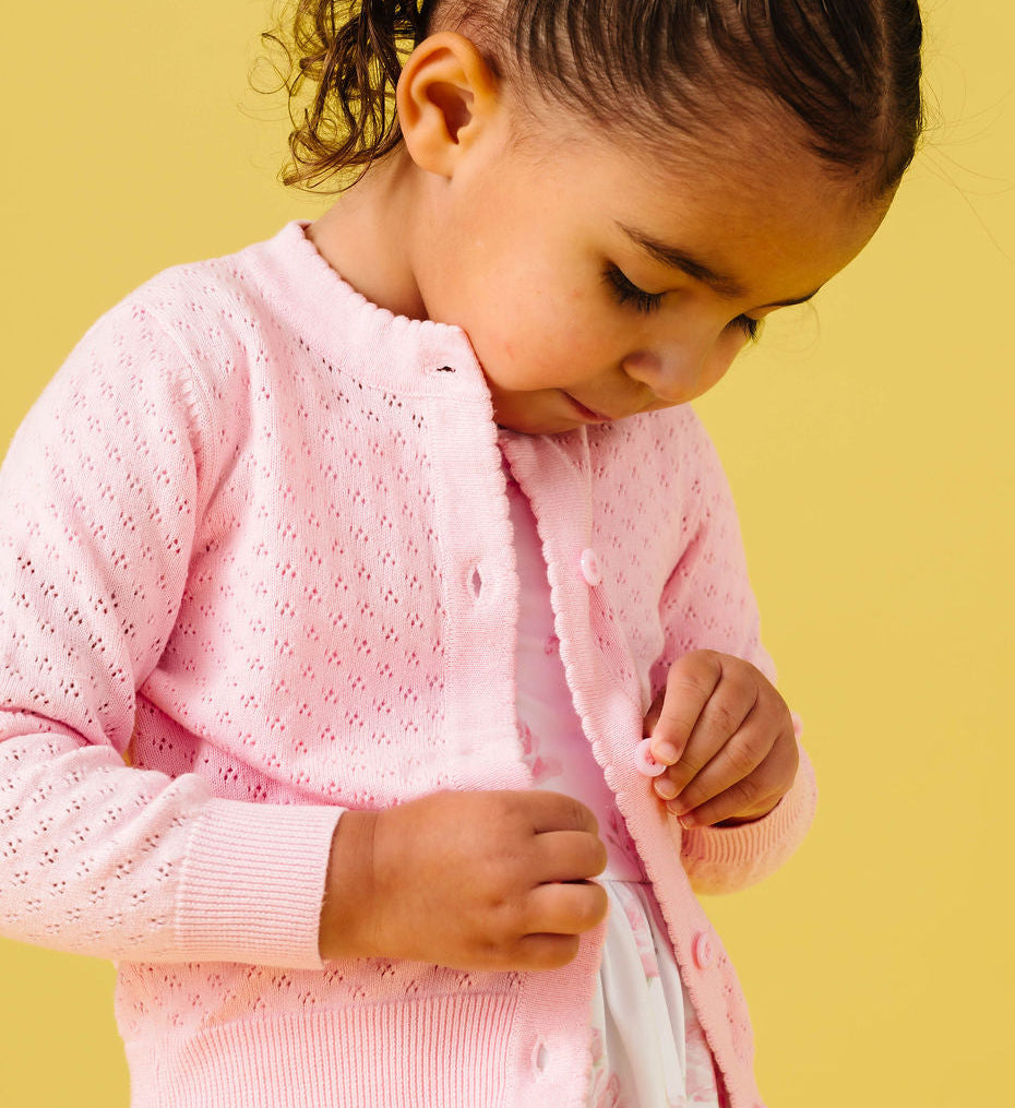 Young girl wearing a pink cardigan over a floral dress against a yellow background