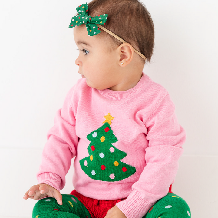 baby in pink knit sweater with Christmas tree detail and matching bloomers, bow and tights