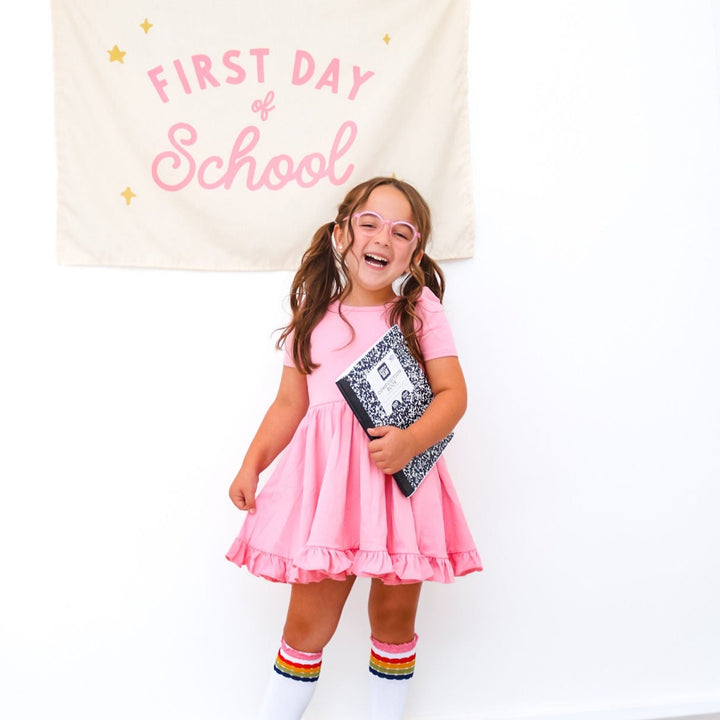 little girl wearing pink twirl dress and rainbow bubble striped knee high socks for first day of school