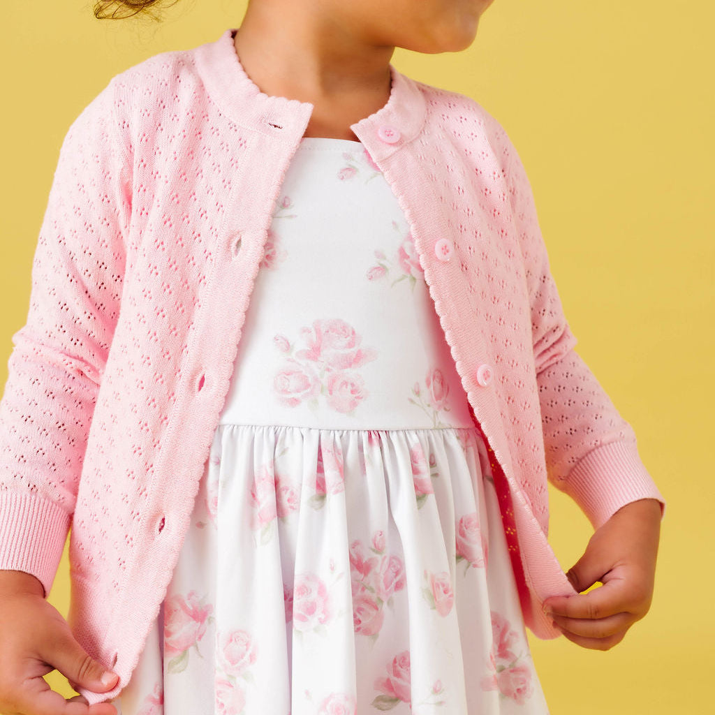 Young girl wearing a pink cardigan over a floral dress on a yellow background