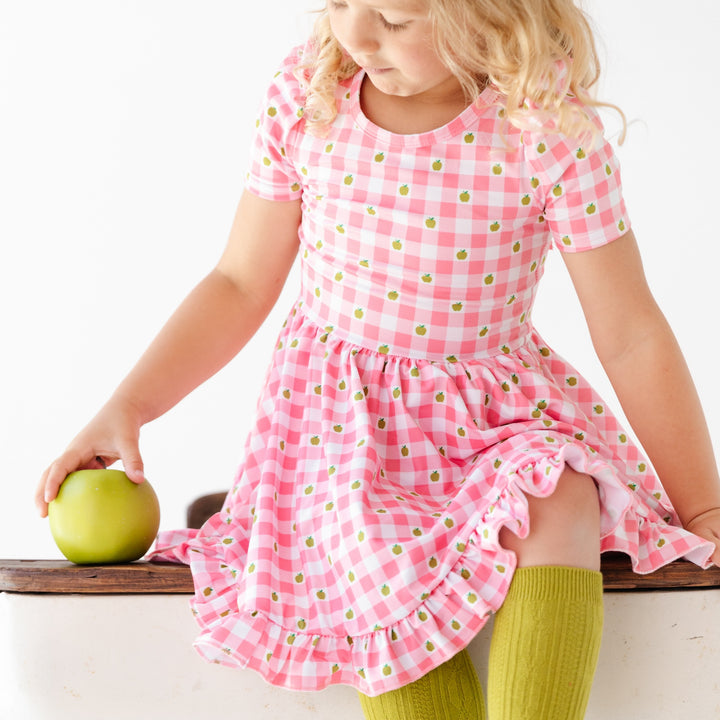 little girl sitting on desk wearing pink gingham back to school dress with green apples