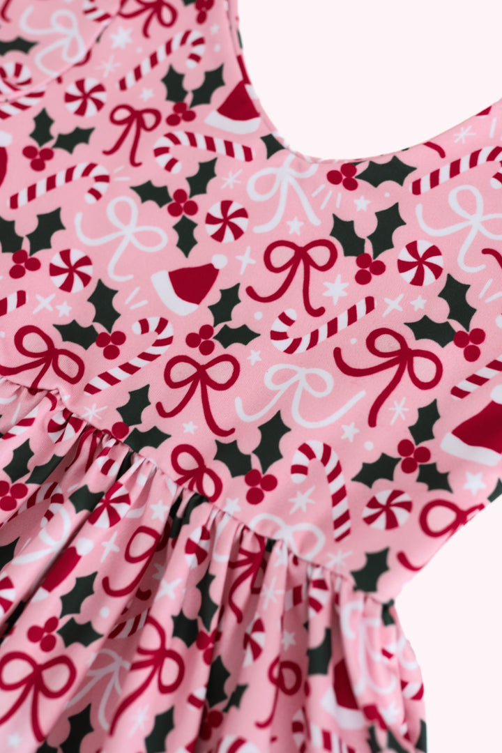 A close-up of a pink holiday-themed fabric with a pattern of red bows, candy canes, holly leaves, and white snowflakes, gathered at the waist.
