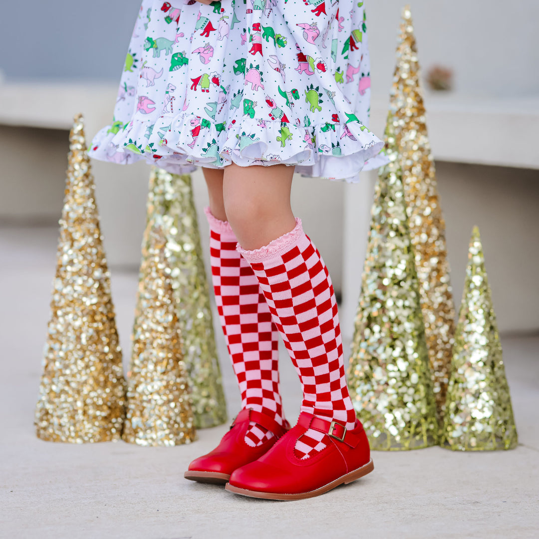 little girl wearing pink and red checker knee high socks with christmas dinos dress