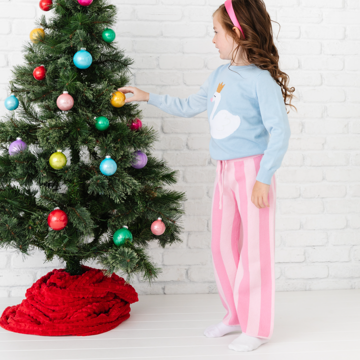 girl wearing pink striped knit pants and blue swan sweater at christmas