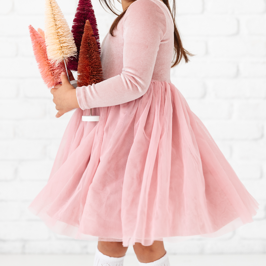 little girl holding Christmas trees in pastel pink velvet dress with tulle skirt