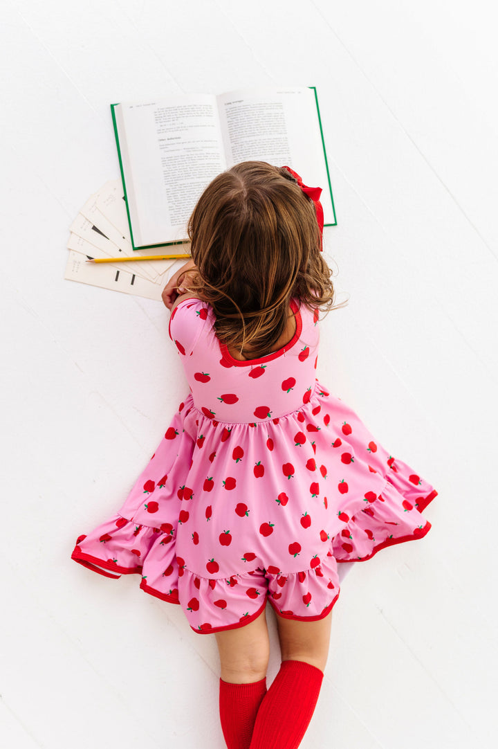 Little girl in pink and red apples dress reading a book