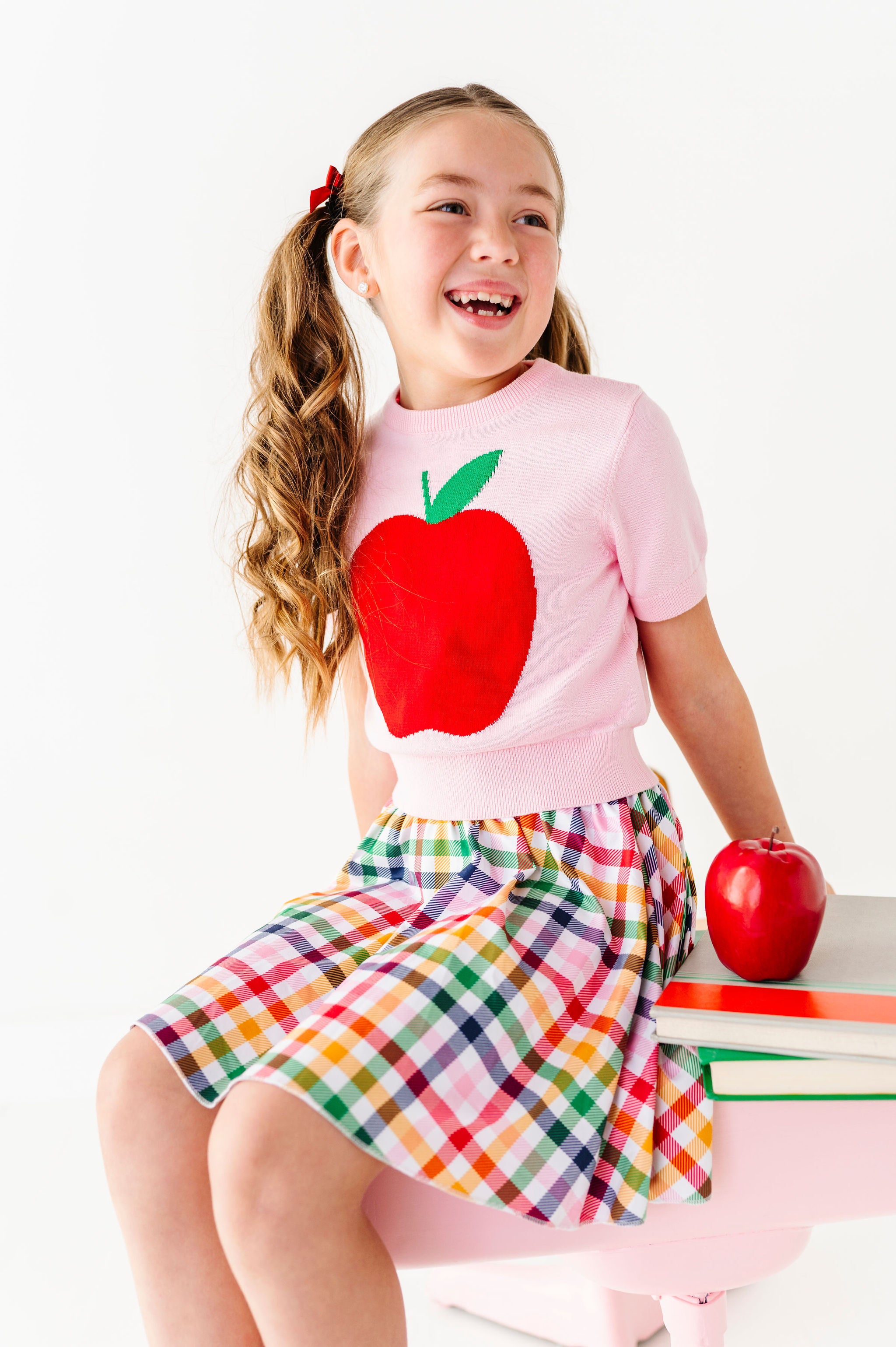 girl wearing pink top with big red apple and rainbow plaid skort for back to school