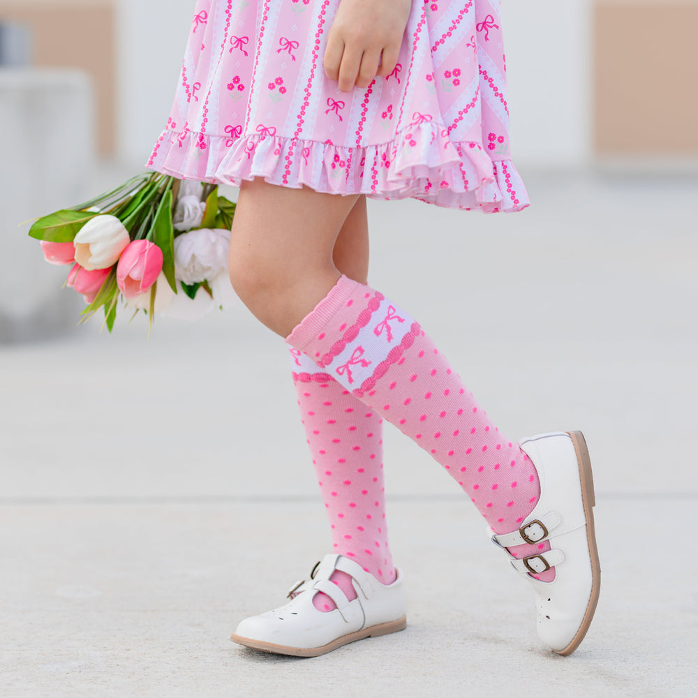little girl in pink wallpaper print spring twirl dress and matching pink scalloped knee highs with polka dots and printed bows