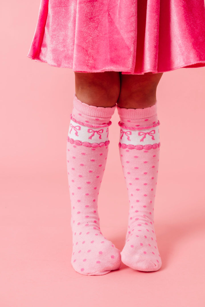 little girl in pink velvet skort and matching pink knee high socks with polka dot and bow design