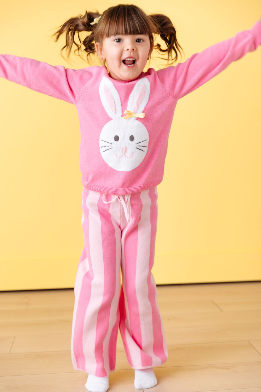 little girl hopping in pink knit easter sweater with white bunny design and matching pink striped sweater pants