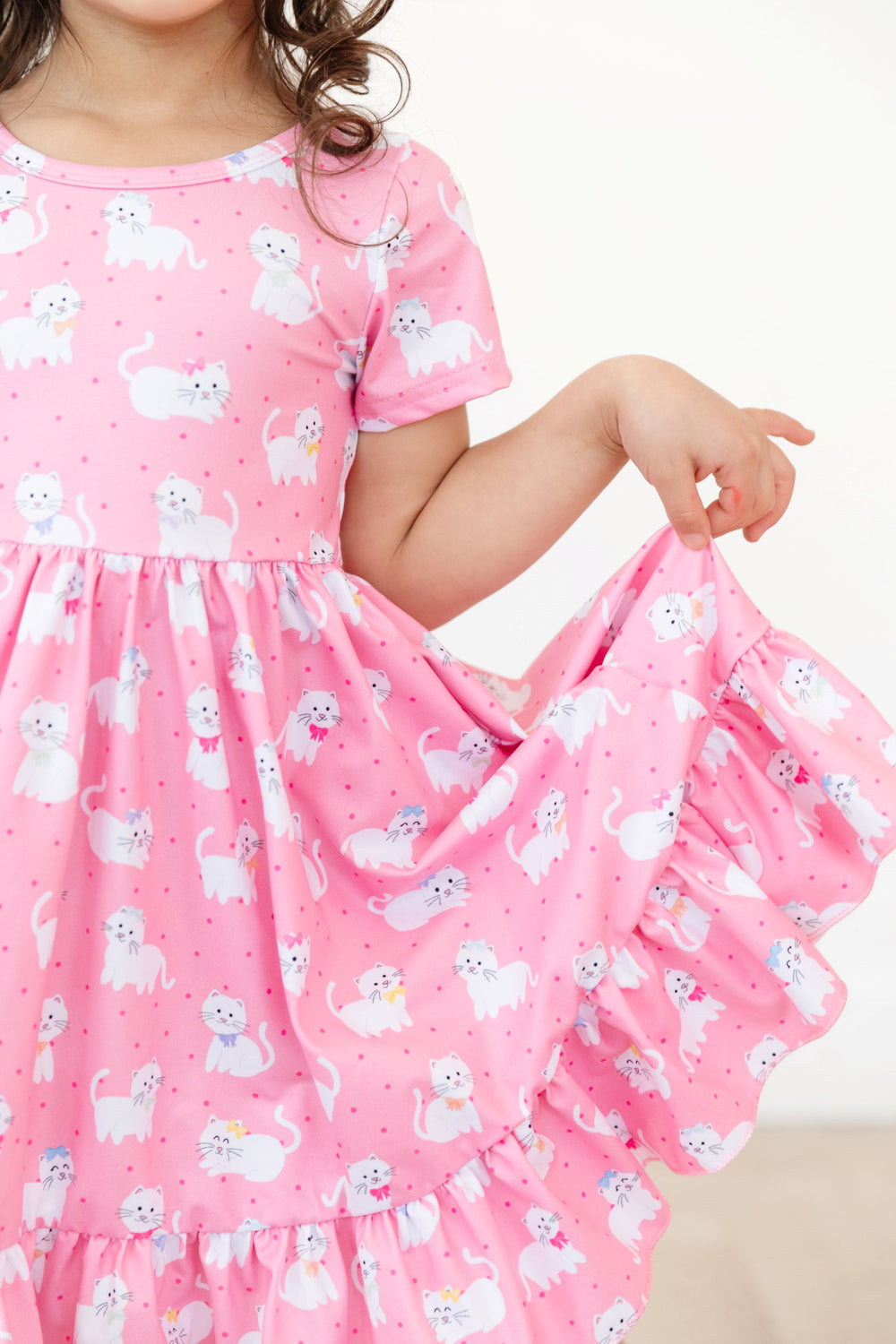 little girl in short sleeve pink dress with white cats in bows showing ruffle trim