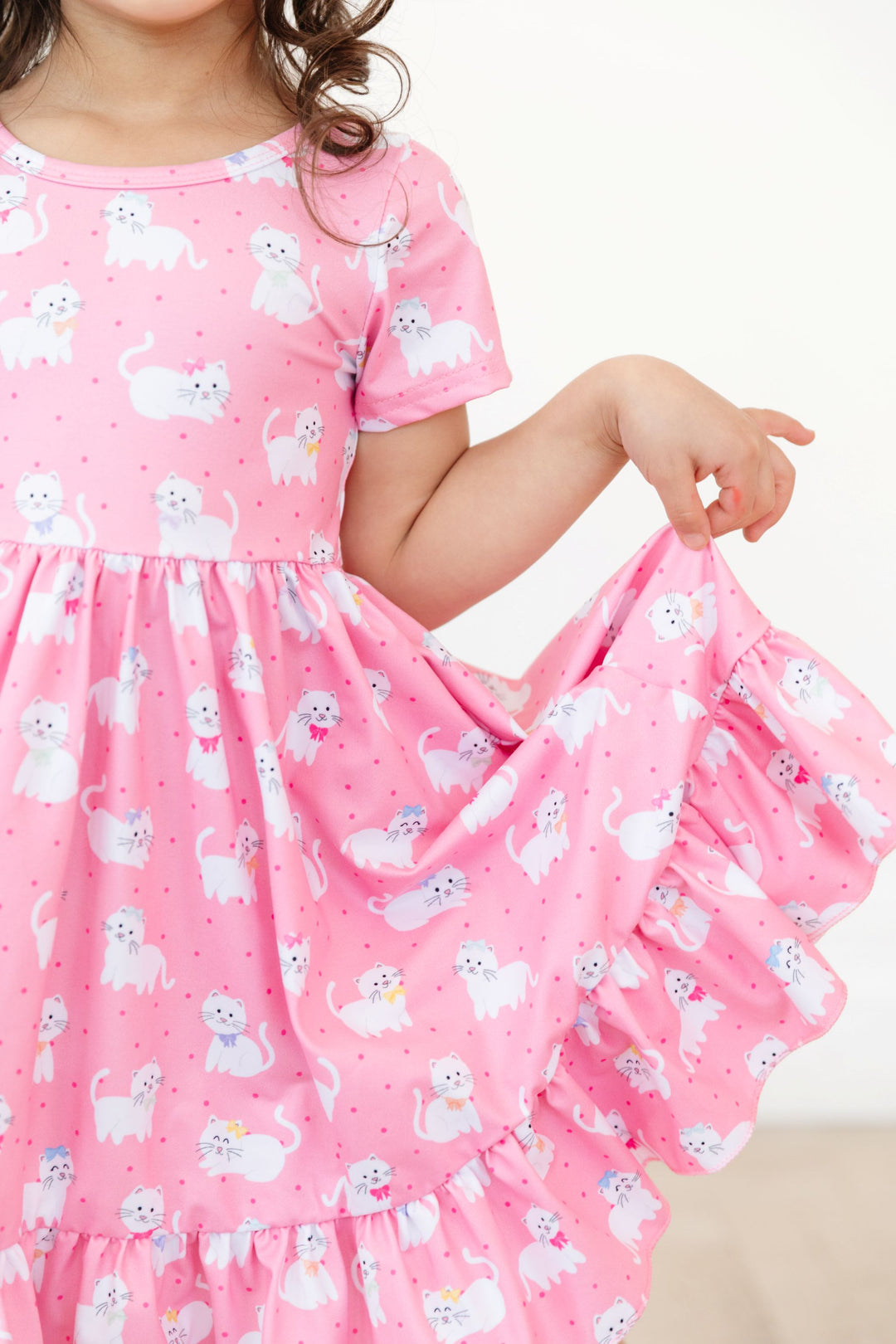 little girl in short sleeve pink dress with white cats in bows showing ruffle trim