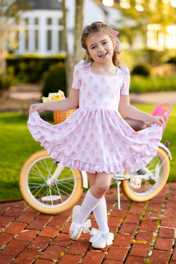 little girl with bike wearing pink spring daisy print twirl dress with white cable knit knee socks