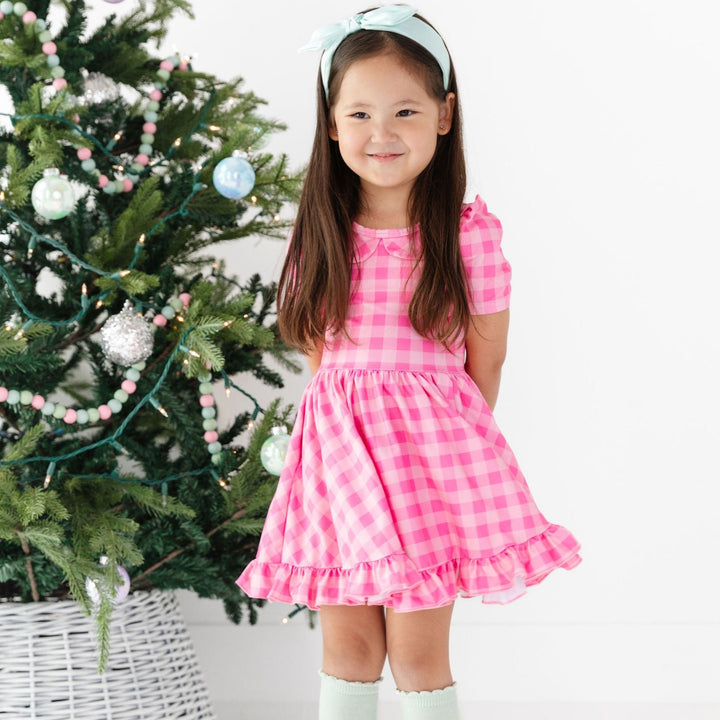 girl wearing pink gingham dress with mint green knee high socks in front of christmas tree