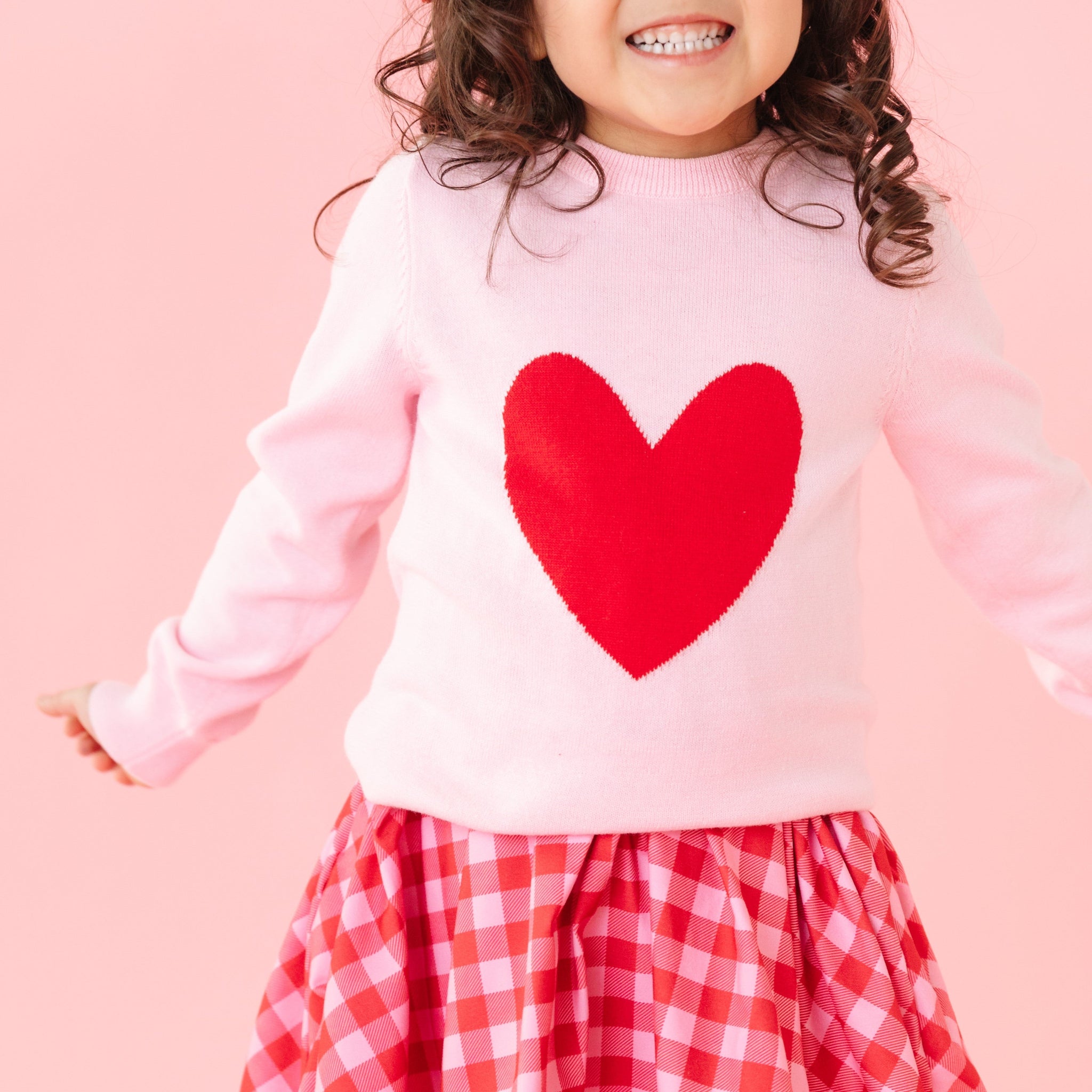 closeup of little girl in pink knit sweater with red heart design paired with red and pink gingham twirl dress