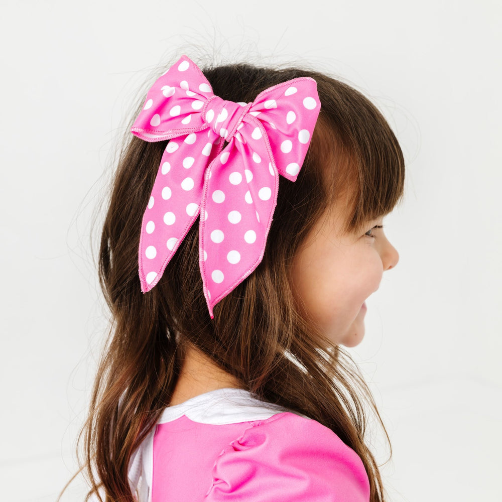 little girl wearing pink polka dot minnie inspired dress with matching pink and white polka dot fabric hair bow on clip