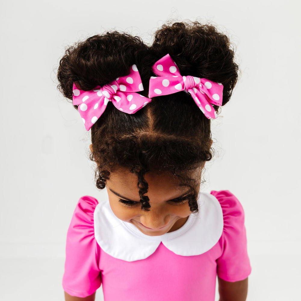 little girl wearing pink fabric bows with white polka dot print to match pink minnie inspired twirl dress 