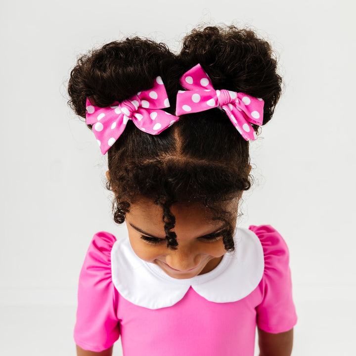 little girl wearing pink fabric bows with white polka dot print to match pink minnie inspired twirl dress 